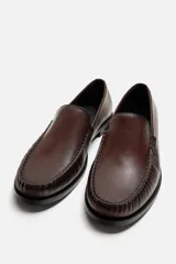 Mocasín de vestir color marrón oscuro, con capellada de cuero, suela a contraste y ligero tacón.