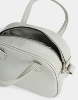 Cartera bowling color gris claro de cuerina con doble asa corta de mano, correa regulable y cierre superior.