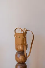 Cartera tipo canasta color terracota con textura símil piel de cocodrilo, con forro de tela blanca ajustable con cordón. Tiene correa larga de cuero marrón con hebilla dorada.