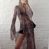 Vestido largo de gasa transparente con estampado de piel de serpiente en tonos marrones. Tiene cuello camisero, mangas largas acampanadas y abertura frontal con cordones.
