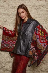 Chaqueta negra de cuero con corte clásico, cuello camisero, cierre frontal con botones y bolsillos con solapa en el pecho. Las mangas son tejidas en lana con diseño geométrico en tonos rojo, marrón, blanco y azul.