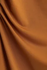 Vestido midi color ocre, sin mangas, de punto elástico con leve brillo. Modelo ajustado con frunces en escote, hombros y en un lateral de la cintura para crear un efecto drapeado.