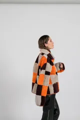 Buzo tipo anorak de cuero genuino, reversible, con diseño de parches en tonos marrones, naranjas y grises. Presenta cuello con solapas y cierre parcial frontal. El forro interior es de pelo sintético en tonos naranja y marrón oscuro.