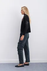 Pantalón cargo color verde oscuro, de corte recto y tiro medio, con ajuste en los tobillos. Confeccionado en gabardina elastizada, cuenta con un cinturón interno y hebilla marcaria que permiten ajustar la cintura. Tiene 2 bolsillos en cada lateral y cierres metálicos en la botamanga.