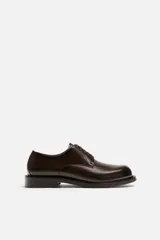 Zapato de vestir tipo derby, color marrón oscuro, con cordones, capellada de cuero brillante, forro y plantilla de cuero y suela plana.