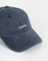Gorra de béisbol azul denim con efecto lavado y bordado frontal con la palabra "Tokyo" en blanco. Ajuste trasero con hebilla metálica.