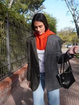 Blazer oversize con diseño asimétrico que combina dos tweeds contrastantes: uno marrón liso y otro blanco y negro con estampado pata de gallo. Tiene botones de strass y un pin de salchicha.