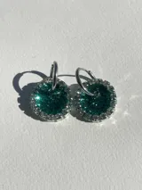 Par de aros colgantes con dije circular de resina color verde esmeralda con glitter, bordeado con strass plateado y arito de acero quirúrgico.