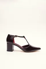 Sandalia de cuero color bordó, con acabado charolado, punta fina y tacón cuadrado de 5 cm. Presenta una tira en forma de T sobre el empeine y una correa con hebilla alrededor del tobillo.