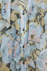 Camisa de cuello redondo y escote pico con estampado floral en tonos celeste, amarillo y negro. Manga larga abullonada acabada en puño. Detalle de volantes en el frente. Cierre frontal con botones.