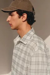 Camisa blanca con diseño a cuadros grises, de corte holgado, manga larga y cuello inglés.