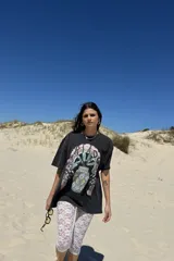 Remera de manga corta, color gris oscuro con efecto lavado, con un estampado frontal que incluye un diseño de planta en una maceta decorada, serpientes y texto. Se usa superpuesta a una remera de manga larga a rayas amarillas y blancas.