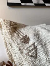 Manta de lana color crudo con bordados de flechas en color marrón.