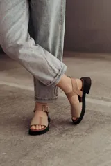 Sandalias bajas color arena, con tiras anchas de cuero y hebilla lateral.