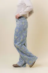 Pantalón de jean de tiro medio-alto, pierna ancha y lavado celeste claro, con estampado floral en tono amarillo pálido.