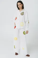 Camisa blanca de lino con corte raglán, detalles desflecados y apliques de frutas tejidas a crochet. Abertura trasera con botones.