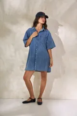 Vestido camisero corto de denim celeste, con cuello clásico, manga corta y cierre frontal con botones.