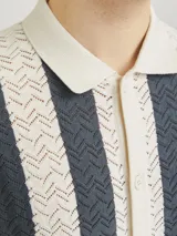 Polo de hombre con tejido texturizado a rayas verticales color crema y gris, corte holgado, cuello tipo polo, mangas cortas y cierre con botones.