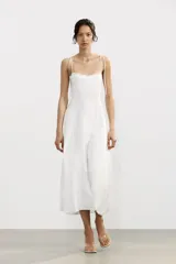 Vestido midi blanco de popelín con escote corazón y volantes. Tiene tirantes finos con detalle de lazo, forro interior combinado y cierre lateral con cremallera oculta.