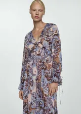 Vestido largo de gasa con estampado paisley en tonos celeste, marrón y rosa. Tiene escote en V con volantes, mangas largas con puños elásticos y lazos, y forro interior.