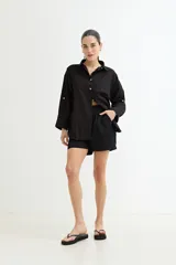 Camisa blanca de corte amplio, con cuello clásico, cierre frontal con botones y mangas largas con puños abotonados.