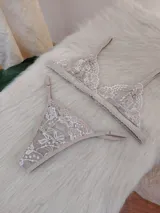 Conjunto de lencería color nude, compuesto por un bralette triangular de encaje floral con tirantes finos y una tanga regulable clásica de encaje a juego.