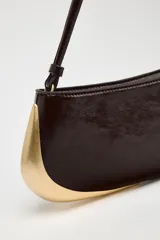 Bolso de hombro alargado color marrón oscuro con detalle metálico dorado en un lateral, asa corta y cierre de cremallera.