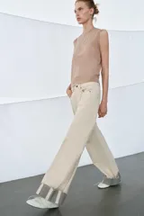 Jeans de tiro medio color beige, corte relaxed leg y largo al tobillo. Cuentan con cinco bolsillos y bajo con vuelta a contraste en gris. Cierre frontal con cremallera y botón.