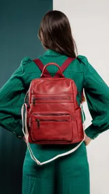 Mochila negra de símil cuero con apertura superior y tres bolsillos frontales con cierres metálicos. Incluye bolsillos laterales y tres bolsillos internos. Tiene correa larga de galón regulable para usar como bandolera y correas para colgar en la espalda.
