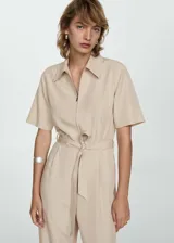 Mono color beige de lino y lyocell, con manga corta, cuello camisero, cierre frontal con cremallera, lazo ajustable en la cintura y bolsillos laterales.