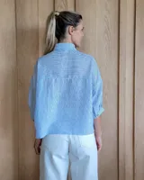 Camisa color beige con rayas verticales blancas, cuello clásico, mangas 3/4 y bolsillos frontales cuadrados.