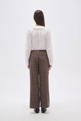 Pantalón de poliéster con estampado de cuadros escoceses en tonos marrón y beige. Presenta un corte ancho y tiro bajo, con pliegues frontales.