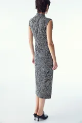 Vestido midi negro con estampado de manchas blancas, sin mangas, de punto elástico, corte ajustado, cuello alto y costura curva fruncida en un lateral para conseguir un efecto drapeado que realza la figura.