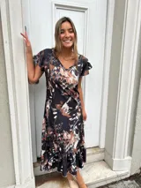 Vestido midi negro con estampado abstracto en tonos beige y blanco, mangas cortas con volados y falda con volados en el ruedo.