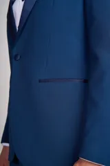 Traje de vestir azul con solapa de satén, compuesto por saco con cierre de un botón, pantalón de corte entallado y moño de satén azul.