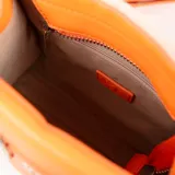 Cartera mini tipo tote bag bicolor, con cuerpo de tela color beige y solapa frontal de cuero sintético color naranja. Tiene doble asa de mano, correa larga regulable y herrajes plateados. Presenta un bolsillo externo con cierre y dos bolsillos internos, uno con cierre y otro abierto.