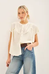 Camisa negra de manga corta con combinación de tejido de punto y plano, detalles de volados y frunces en pechera y espalda, acceso con botones fake nacar y medallita marcaria en espalda.