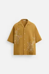 Camisa color ocre de corte relaxed fit, confeccionada en tejido con mezcla de algodón y lino. Tiene cuello bowling, manga corta, bordado con abalorios en el delantero y cierre frontal de botonadura.