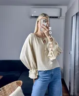 Blusa blanca de mangas largas con volados en los puños y escote con lazo.