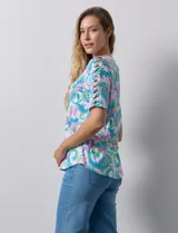 Remera estampada con diseño paisley en tonos celeste, rosa, amarillo y verde. Tiene mangas cortas con detalle de aberturas y lazos en los hombros.
