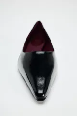 Zapato plano de charol negro con punta fina y suela baja.