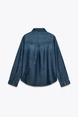 Camisa de denim azul con cuello solapa, manga larga, dos bolsillos delanteros con solapa y cierre frontal con botones a presión.
