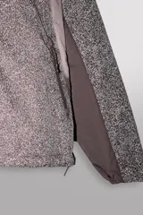Cazadora marrón de tejido técnico ligero con partículas reflectantes. Tiene cuello alto con capucha elástica, mangas largas con puños elásticos, bolsillos frontales con cremallera en pecho y cadera, y cierre frontal con cremallera. Pertenece a la línea Zara Athleticz.