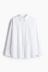 Camisa blanca de popelina de algodón, corte amplio, con cuello clásico, cierre frontal con botones, canesú en la espalda, hombros caídos, bolsillo de parche en el pecho, mangas largas con puños abotonados y bajo redondeado con aberturas laterales.