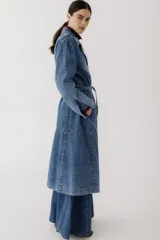 Tapado largo de jean azul con doble botonadura, cuello clásico, mangas largas abullonadas y cinturón de lazo.
