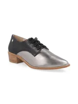 Zapato acordonado de cuero color plateado con puntera fina y detalle de cuero marrón en el talón.