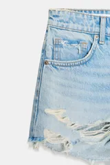 Short de jean de tiro alto, color celeste claro desgastado, con roturas grandes y deshilachado en el bajo. Presenta cinco bolsillos y cierre frontal con botón metálico.