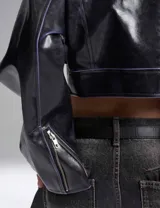 Campera corta de cuero sintético negro con cierre cruzado, cuello con solapas y cinturón con hebilla.