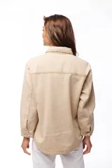Sobrecamisa de jean color beige, con cuello clásico, cierre frontal con botones y dos bolsillos de parche en el pecho.