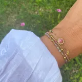 Pulsera dorada de acero con cadena de eslabones y tres dijes circulares: uno central con piedra rosa y dos laterales con diseño calado.